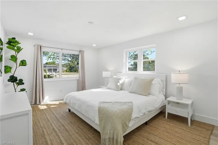 Bright bedroom featuring two windows with white frames, recessed lighting, wood-finish flooring, and white baseboards