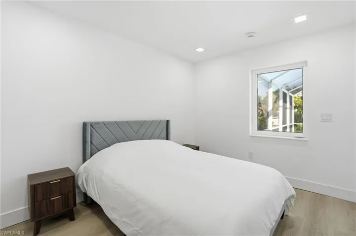 Neutral white walls and light wood-finish flooring define this bright room, featuring recessed lighting and a single window