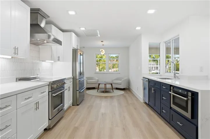 Modern kitchen featuring light wood-finish flooring, two-tone cabinetry with white upper and dark lower units, stainless steel appliances, and white countertops