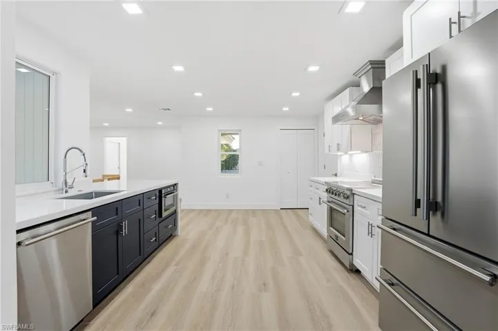 Modern kitchen featuring a large island with sink and microwave, stainless steel appliances, white cabinetry, and light wood-finish flooring