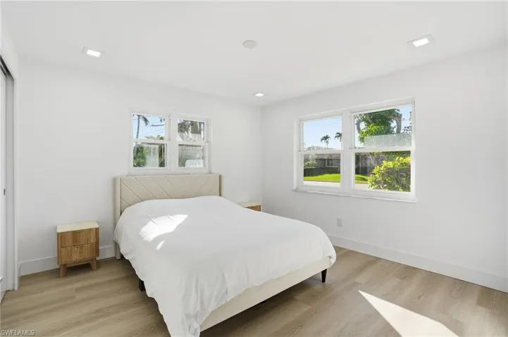 Bright interior space featuring light wood-finish flooring, white walls, and a pair of windows providing ambient light