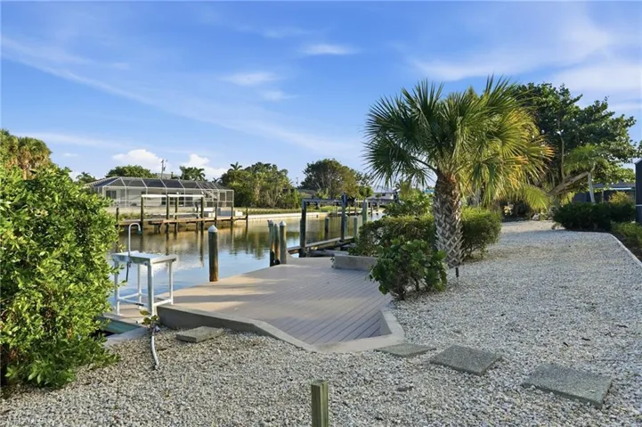 Waterfront property featuring a composite dock, boat lift, palm tree landscaping, and a gravel pathway