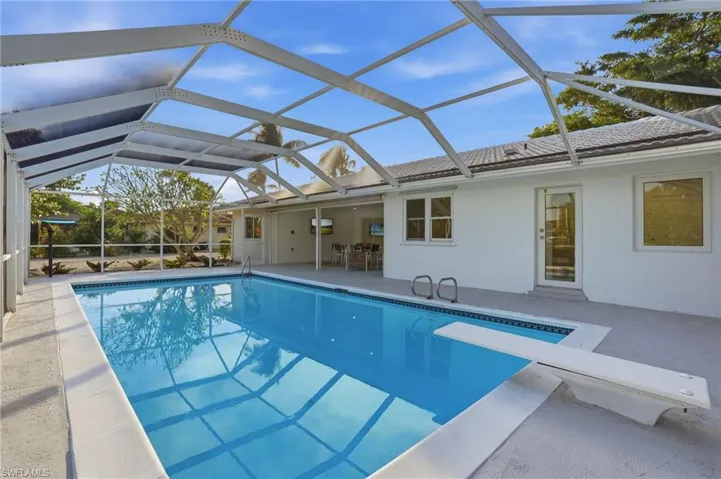 Screened-in pool area featuring a rectangular pool with a diving board, light gray concrete decking, and a white stucco exterior