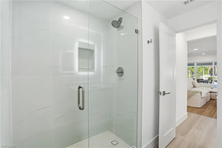 Glass-enclosed shower featuring white large-format wall tiles with subtle veining, a built-in shower niche with accent tiling, a rainfall showerhead, and a hexagonal tile floor