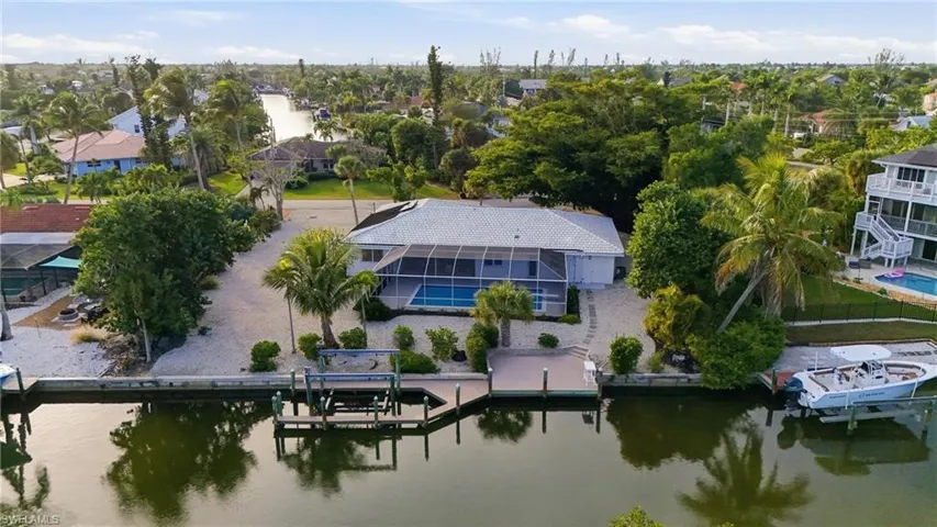 Waterfront property featuring a screened-in pool, private dock, boat lift, direct canal access, and mature landscaping
