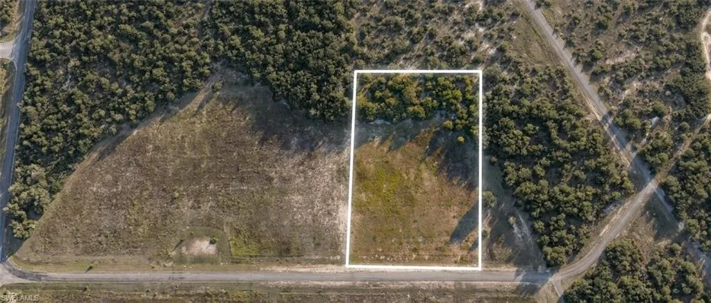 Aerial view of a rectangular parcel of land, bordered by a partially paved road