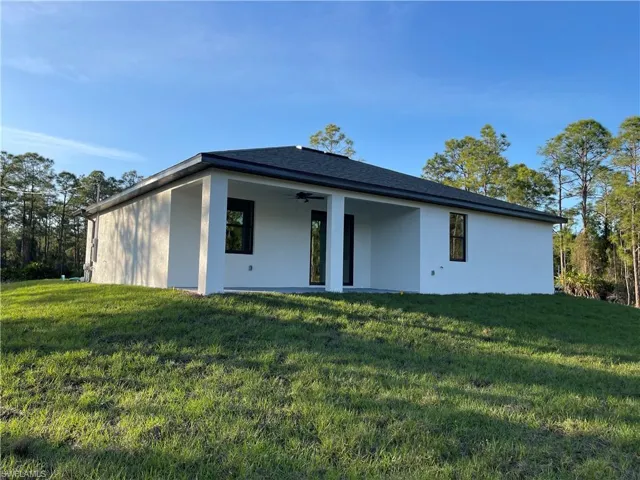 Rear view of house with stucco siding, a lawn, and ceiling fan