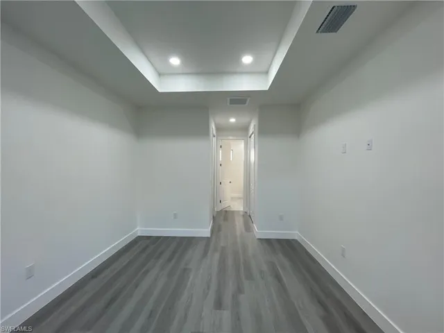 Unfurnished room with a raised ceiling, dark wood-style floors, recessed lighting, and baseboards