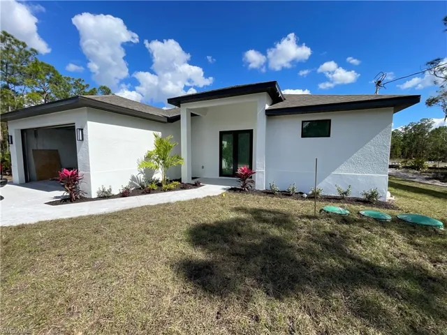 View of front of house with stucco siding, an attached garage, a front yard, french doors, and concrete driveway