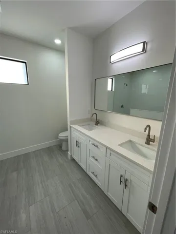Bathroom with toilet, double vanity, baseboards, and recessed lighting