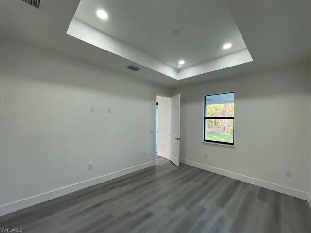 Empty room featuring a tray ceiling, dark wood finished floors, baseboards, and recessed lighting