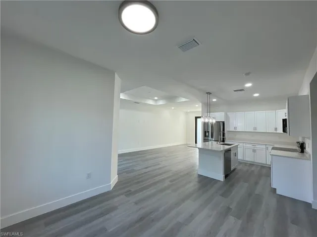 Kitchen featuring open floor plan, baseboards, a center island with sink, recessed lighting, and dishwasher