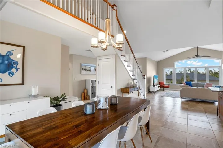Dining space featuring ceiling fan with notable chandelier, light tile patterned floors, and high vaulted ceiling