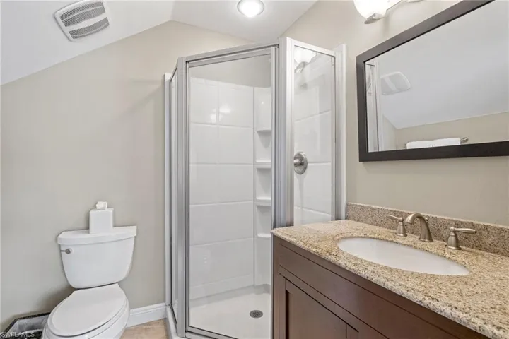 Bathroom featuring vanity, lofted ceiling, toilet, and a shower with door