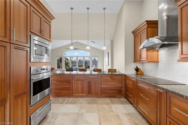 Kitchen with appliances with stainless steel finishes, hanging light fixtures, dark stone countertops, wall chimney exhaust hood, and ceiling fan