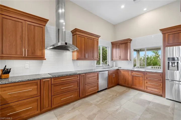 Kitchen featuring tasteful backsplash, sink, stone counters, wall chimney exhaust hood, and stainless steel appliances