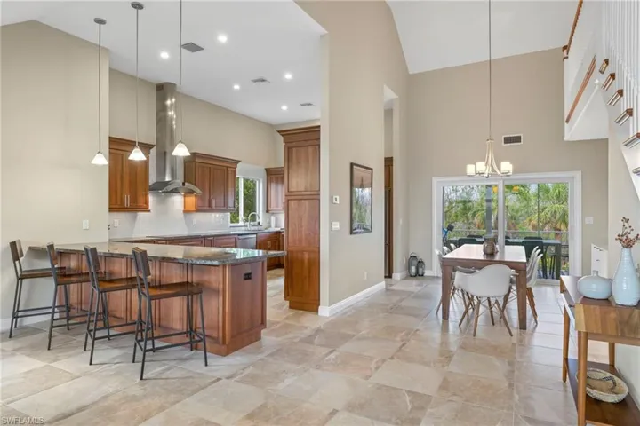 Kitchen with decorative light fixtures, wall chimney exhaust hood, plenty of natural light, and high vaulted ceiling