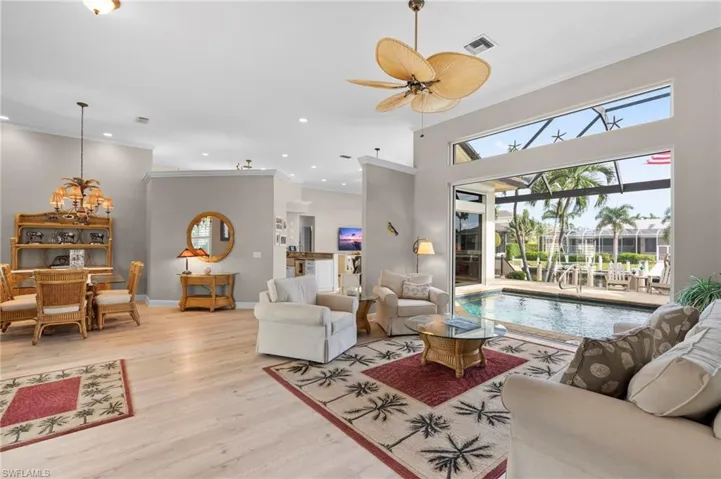 Living room featuring ceiling fan with notable chandelier, light wood-type flooring, and ornamental molding