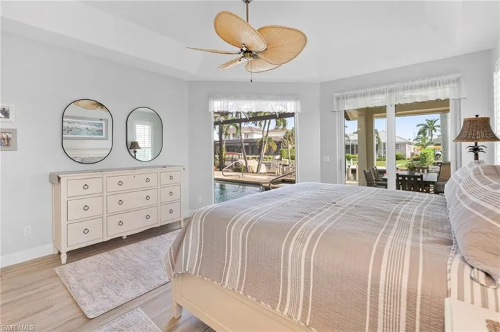 Bedroom featuring access to outside, a tray ceiling, light hardwood / wood-style floors, and ceiling fan