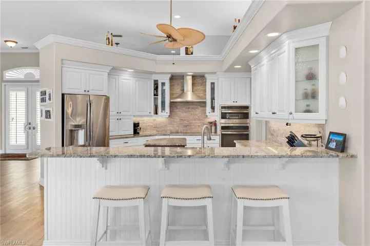 Kitchen featuring ceiling fan, white cabinets, kitchen peninsula, wall chimney exhaust hood, and stainless steel appliances