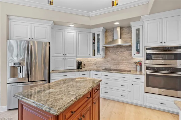 Kitchen featuring appliances with stainless steel finishes, white cabinetry, wall chimney exhaust hood, a center island, and ornamental molding