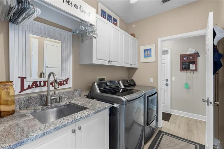 Clothes washing area with ceiling fan, sink, washer and dryer, cabinets, and light hardwood / wood-style floors