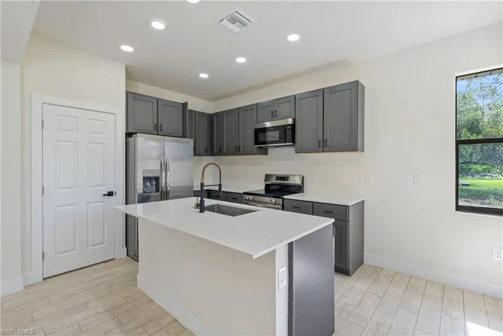Kitchen with stainless steel appliances, light wood-style flooring, recessed lighting, a kitchen island with sink, and light stone counters