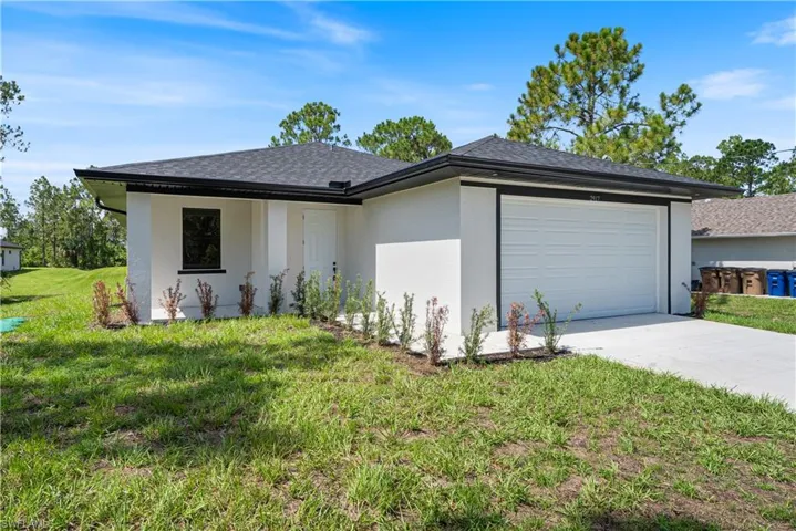 View of front of home with an attached garage, driveway, stucco siding, a front yard, and roof with shingles