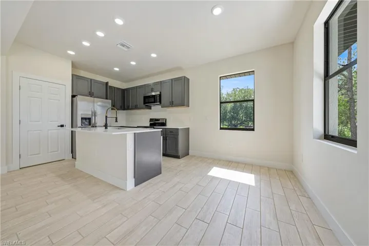 Kitchen with stainless steel appliances, light countertops, light wood-type flooring, recessed lighting, and an island with sink