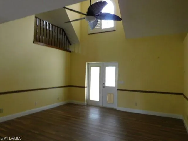 Unfurnished room with a high ceiling, dark wood finished floors, and a ceiling fan