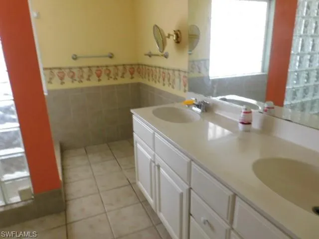 Bathroom featuring light tile patterned flooring, double vanity, tile walls, and a wainscoted wall