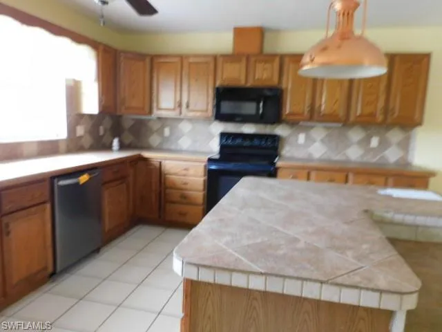 Kitchen with brown cabinets, black appliances, tasteful backsplash, a ceiling fan, and light tile patterned floors
