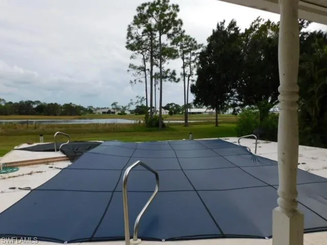 View of pool with a patio, a water view, a covered pool, and a yard