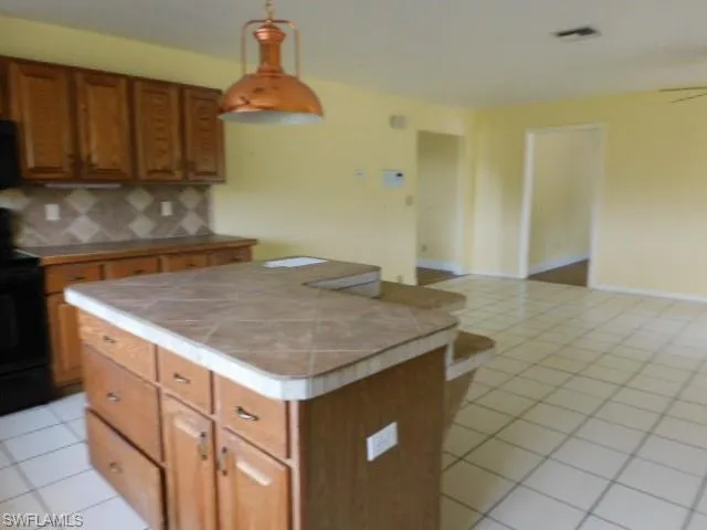 Kitchen with light tile patterned floors, brown cabinetry, tile counters, tasteful backsplash, and black electric range