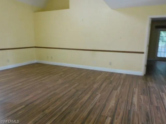 Empty room with dark wood-type flooring and baseboards