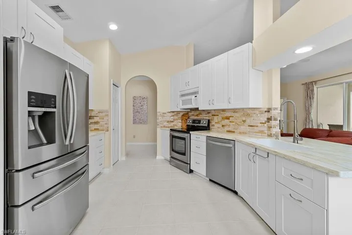 White cabinetry, stainless steel appliances, light-toned countertops, and a tiled backsplash