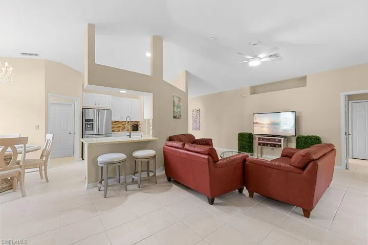 Vaulted ceilings, recessed kitchen, white cabinetry, stainless steel appliances, and tile flooring