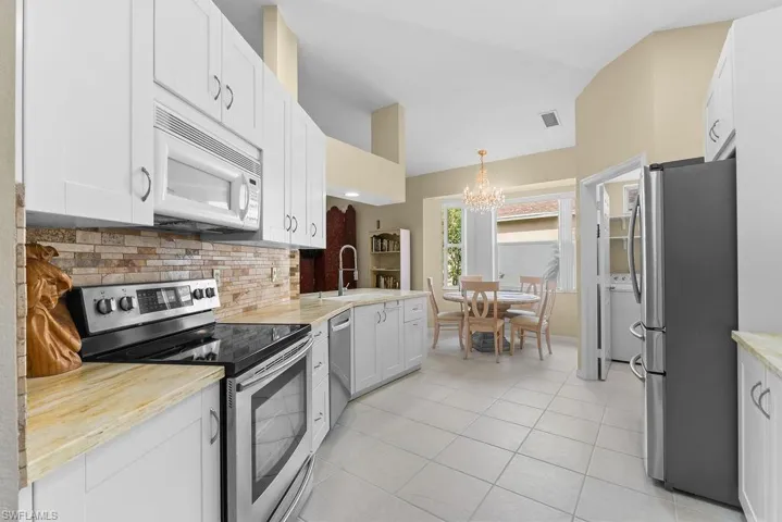 White cabinetry with stainless steel appliances, stone backsplash, and light-toned countertops