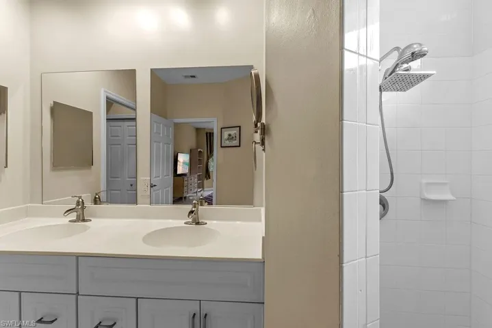 Dual vanity with integrated sinks, brushed nickel fixtures, and white cabinetry. Fully tiled large shower with multiple shower heads.
