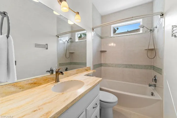 Bathroom featuring a built-in bathtub with shower, a vanity with an integrated sink, a large wall-mounted mirror, and a window