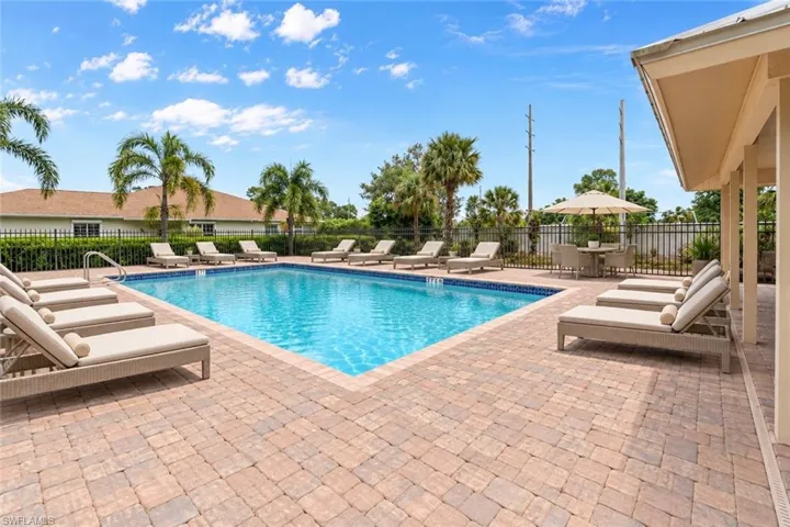 Swimming pool with paver decking, surrounded by a black metal fence and tropical landscaping. AI staging of pool furniture.