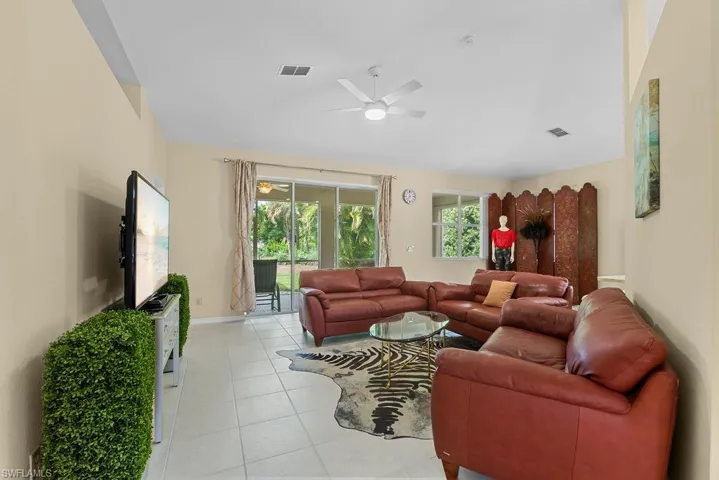 Spacious living area featuring neutral-toned walls, tile flooring, a ceiling fan, and large sliding glass doors leading to an outdoor space