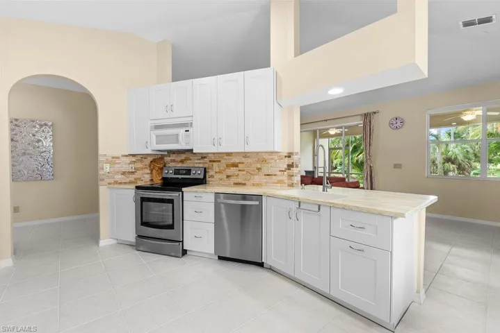 White cabinetry with stainless steel appliances, light-toned countertops, and a stone-finish backsplash