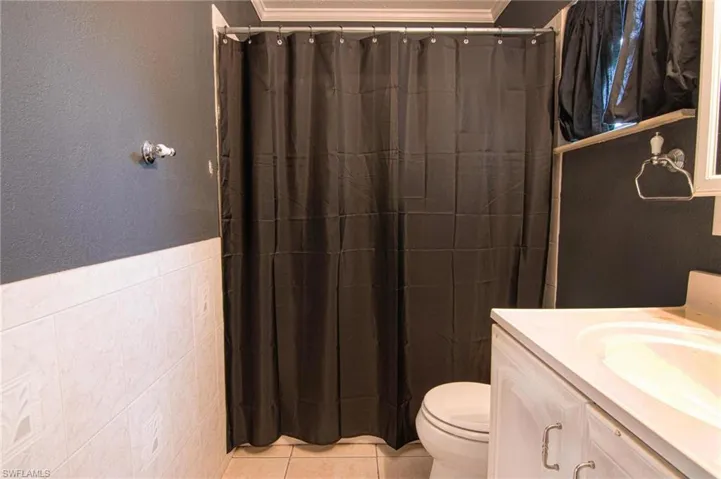 Full bath featuring vanity, a shower with shower curtain, light tile patterned floors, tile walls, and ornamental molding