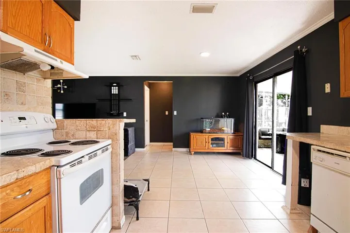 Kitchen with white appliances, decorative backsplash, under cabinet range hood, light tile patterned floors, and brown cabinets