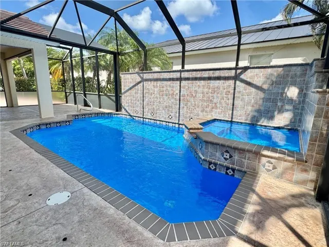 Screened enclosure featuring a rectangular pool with an integrated spa, decorative tile accents, and a textured concrete deck