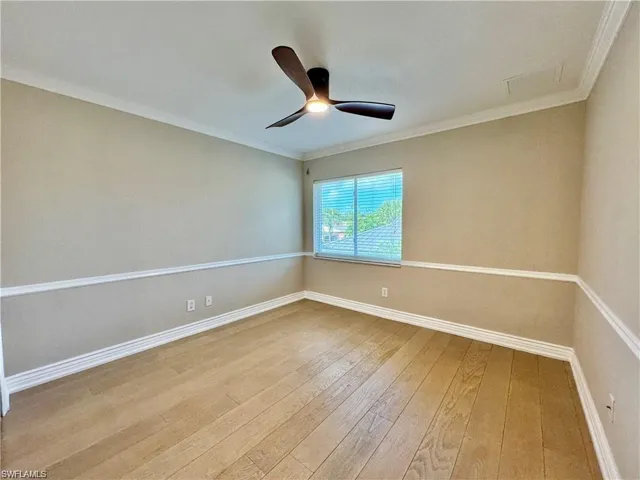 Room featuring wood-finish flooring, neutral wall tones with decorative chair rail molding, and a modern ceiling fan with integrated lighting