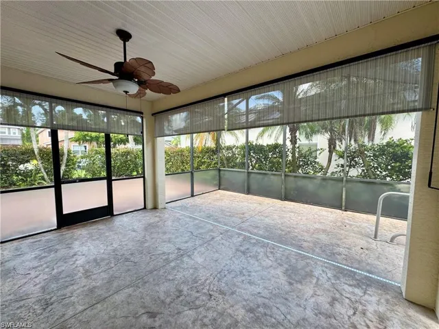 Screened lanai featuring stamped concrete flooring, a ceiling fan with integrated lighting, frosted glass panels, and roll-down shades