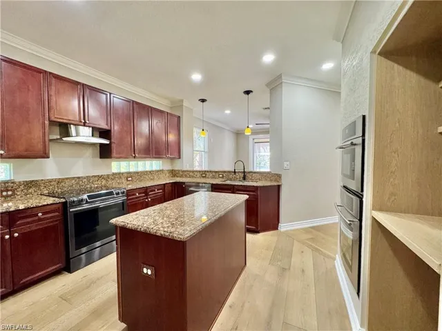 Kitchen featuring wood-finish cabinetry, granite countertops, and stainless steel appliances including a built-in oven stack and a range with overhead hood