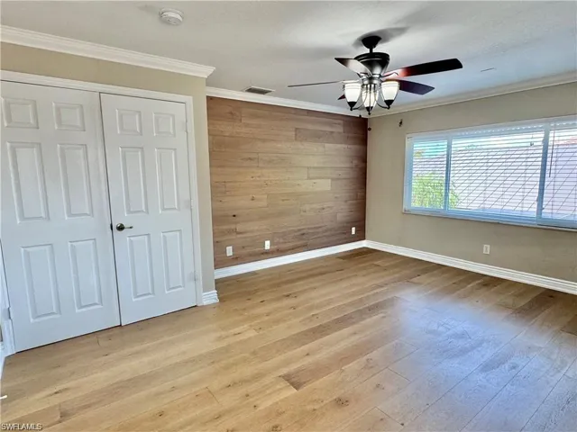 Spacious room featuring wood-finish flooring, a decorative wood-paneled accent wall, a multi-pane window with horizontal blinds, and a ceiling fan with integrated lighting